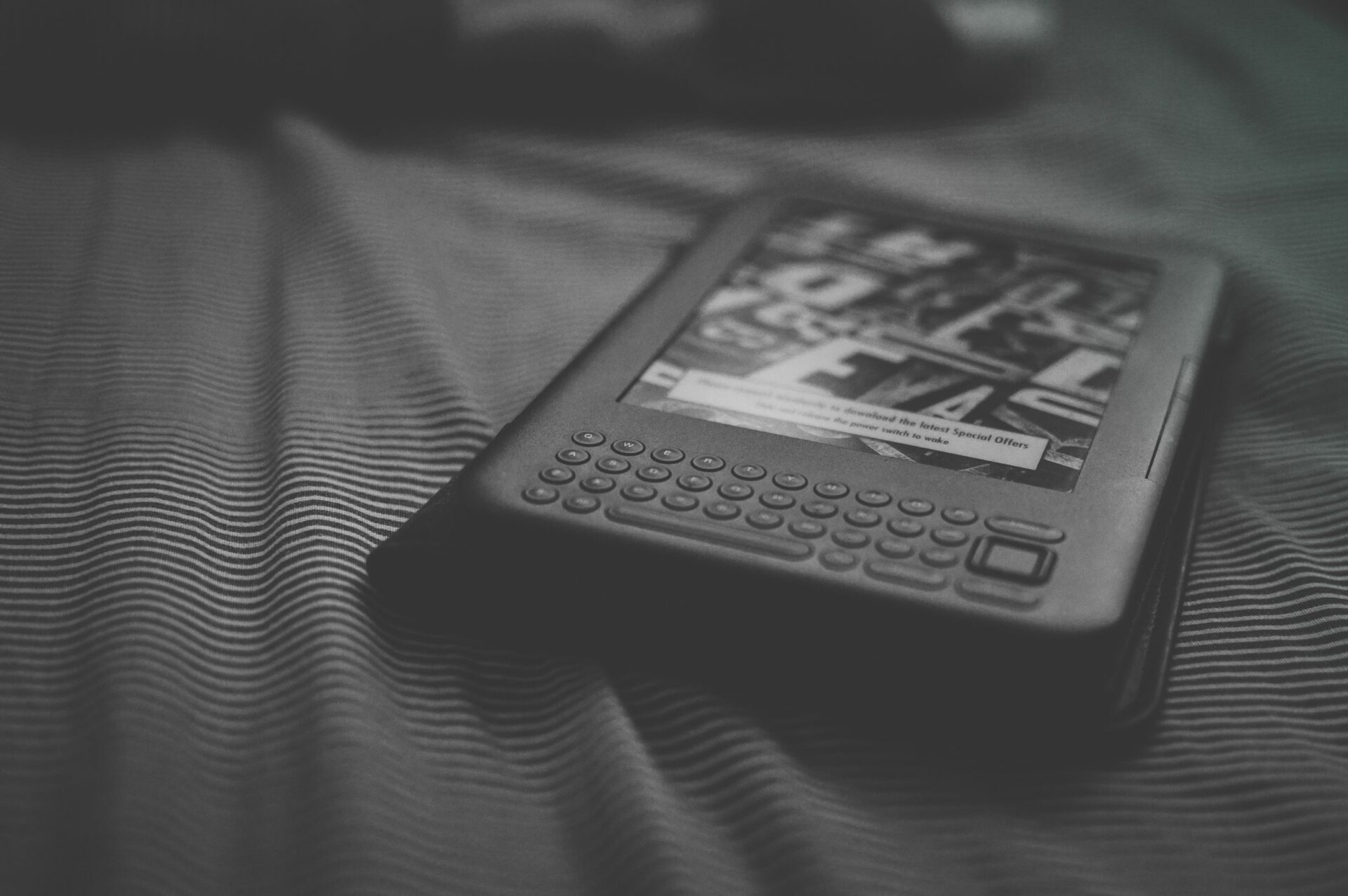 布の上に置かれた、キーボードのついた旧型の電子書籍リーダー（モノクロ写真）